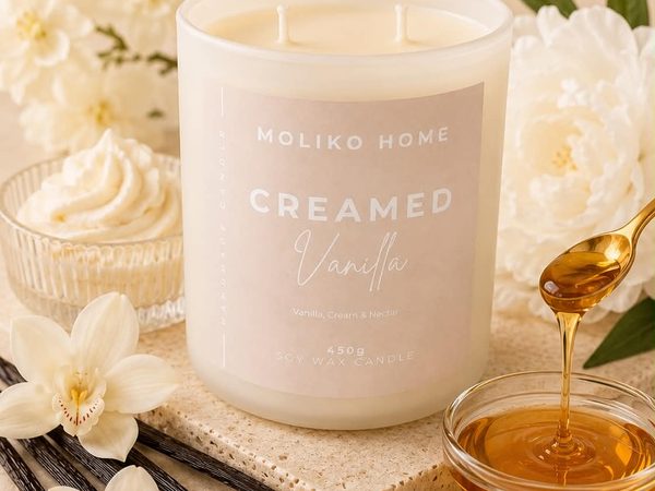 A Moliko Home candle on a stone slab with vanilla flowers, vanilla pods and a spoon of honey.
